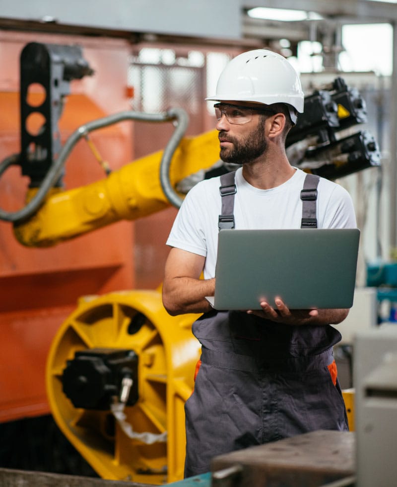 Trabajador en una fábrica utilizando un ordenador portátil cerca de maquinaria robotizada