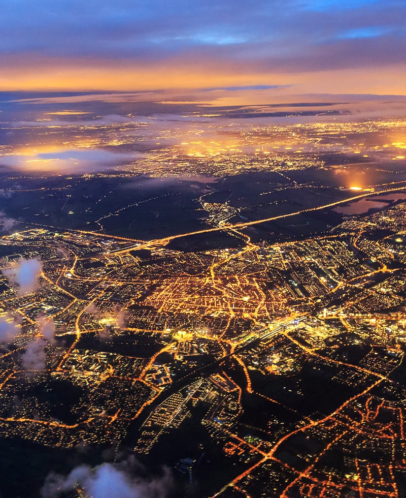 Vista aérea nocturna de la red eléctrica iluminada y la red de calles de una ciudad, que representa la automatización de la red inteligente.